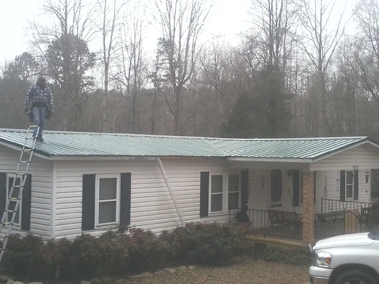 Worker on a ladder beside a new green metal roof on a ranch home in Walterboro