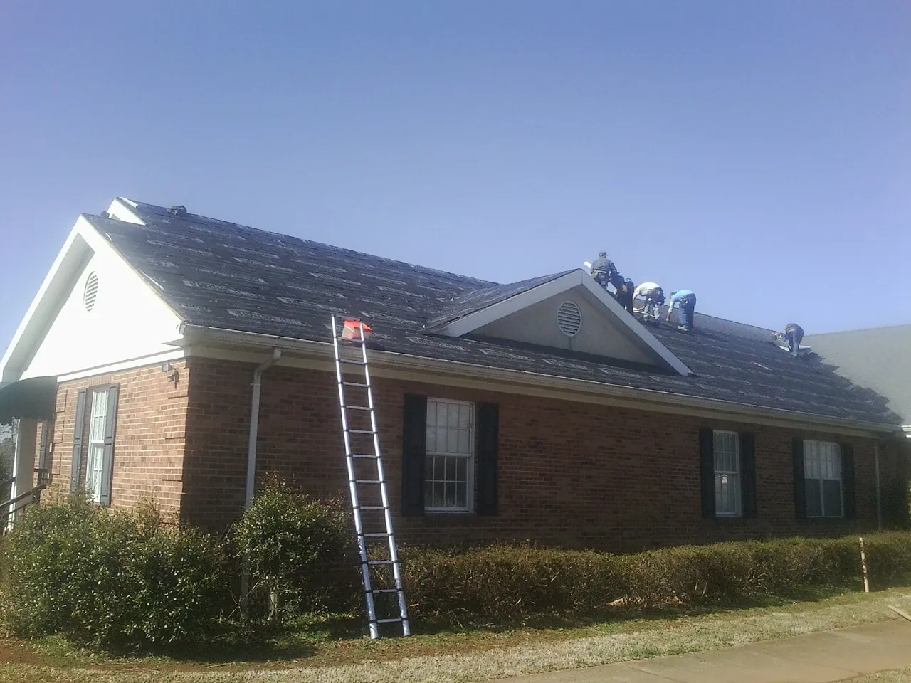 Crew tearing shingles off a brick ranch roof with a ladder set — Metal Roof Repair work by our crew in Walterboro