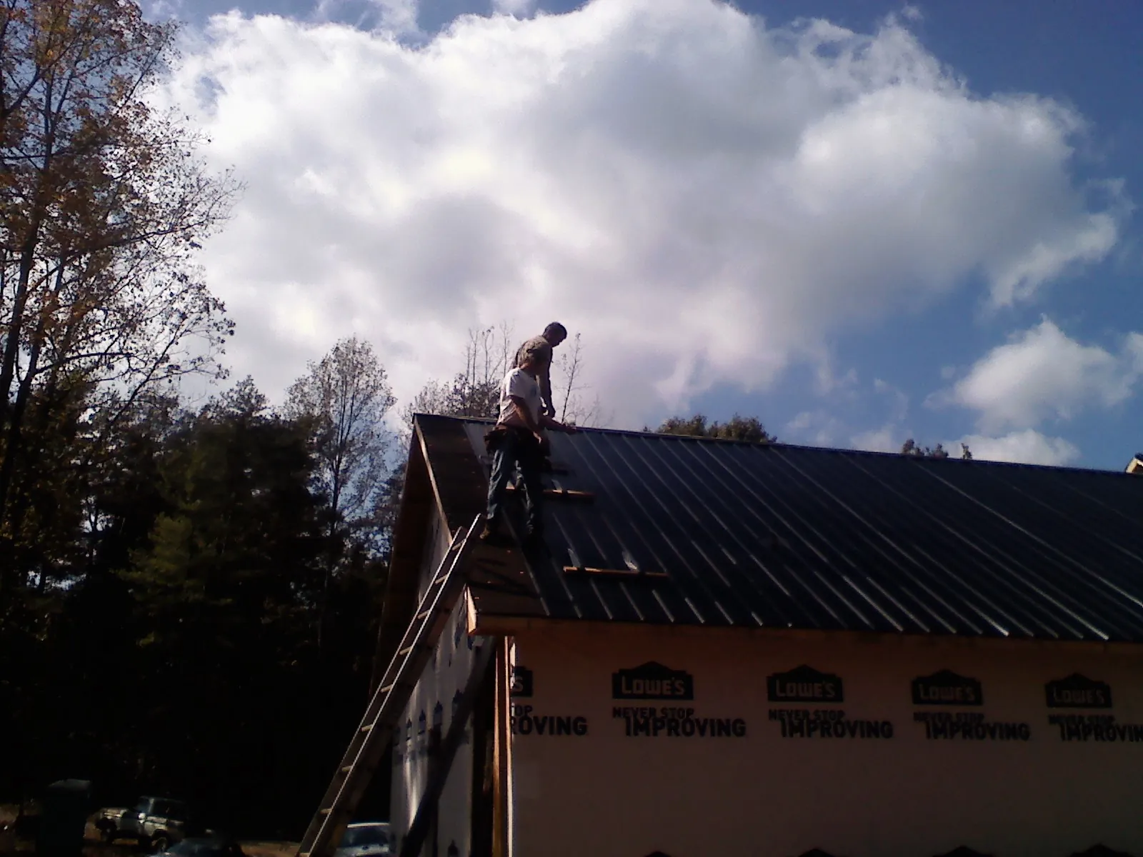 Roofer fastening dark metal panels high against a cloudy sky, from a Roof Inspection job in Walterboro