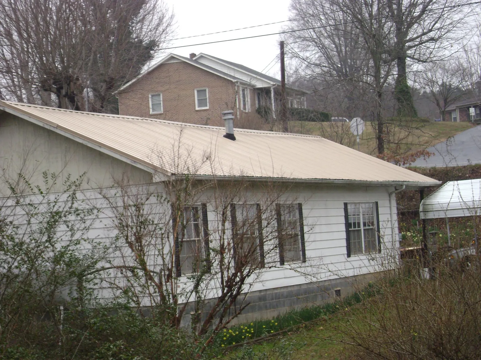 Tan metal roof on a white sided house set into a hillside — Commercial Roofing by Roofing Brothers in Walterboro